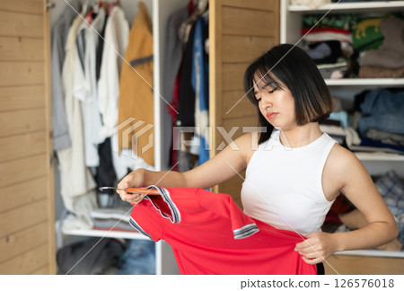 Sad young Asian girl trying to choose a dress standing by wardrobe Sad young Asian girl trying to choose a dress standing by wardrobe 126576018