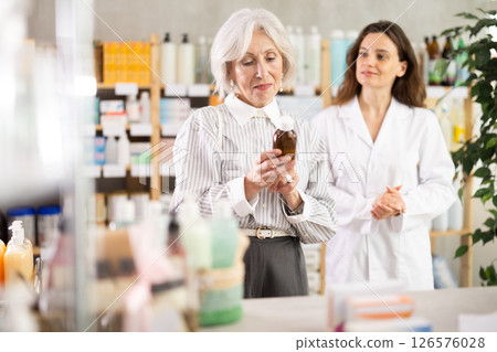 Mature woman choose antitussive syrup, woman pharmacist offers similar item 126576028