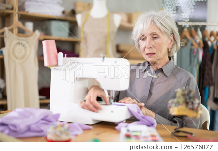 woman dressmaker sews on a machine in a workshop woman dressmaker sews on a machine in a workshop 126576077
