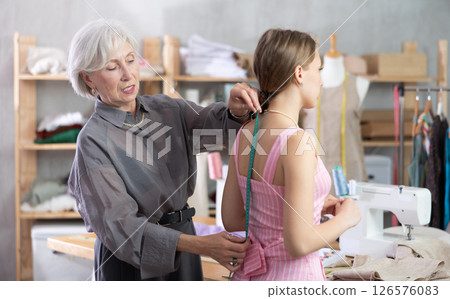 Mature dressmaker measuring client 126576083
