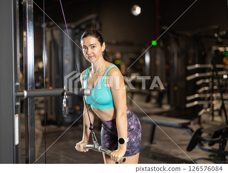Woman performing triceps pushdowns on cable machine in gym Woman performing triceps pushdowns on cable machine in gym 126576084