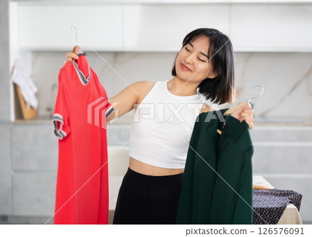 Happy young Asian girl trying to choose a dress in the kitchen Happy young Asian girl trying to choose a dress in the kitchen 126576091