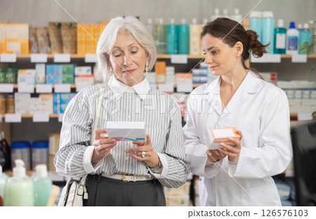 Elderly woman choosing packages of pills and medicines with pharmacist at pharmacy Elderly woman choosing packages of pills and medicines with pharmacist at pharmacy 126576103