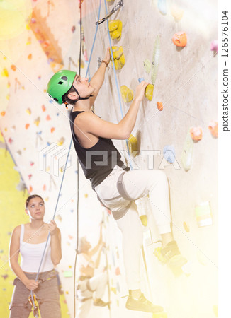 Positive extreme young guy with rope training on concrete climbing rock wall to maintain healthy discipline in indoor adventure park 126576104