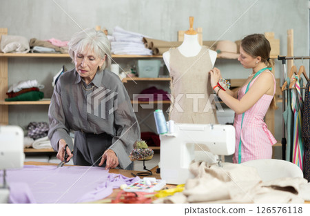 Mature female dressmaker cutting textile other work with mannequin 126576118