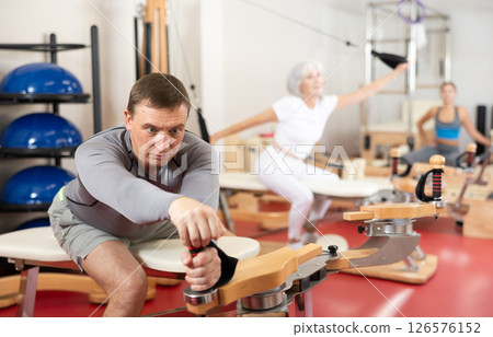 Man during Pilates training performs exercises and tasks on heron pulley tower Man during Pilates training performs exercises and tasks on heron pulley tower 126576152