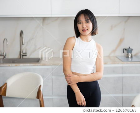 Smiling young Asian girl standing at table in the kitchen Smiling young Asian girl standing at table in the kitchen 126576165