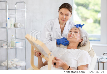 Mature patient with mirror, doctor with gloves Mature patient with mirror, doctor with gloves 126576171