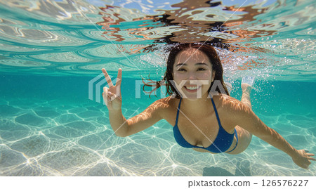 A Japanese woman in a blue bikini swimming underwater while making a peace sign A Japanese woman in a blue bikini swimming underwater while making a peace sign 126576227