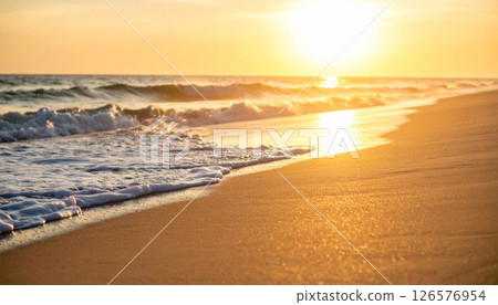 Warm sunlight paints the desert landscape and mountain horizons, with the sun setting over calm ocean waves or rising above sandy beaches under a beautiful sky 126576954