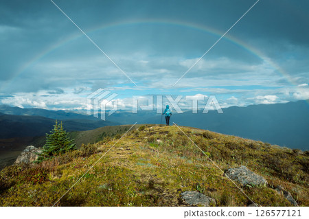 Woman backpacker hiking on high altitude mountain top after the rain,face a beautiful rainbow Woman backpacker hiking on high altitude mountain top after the rain,face a beautiful rainbow 126577121