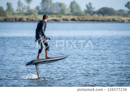 A man glides effortlessly on an electric hydrofoil surfboard 126577236