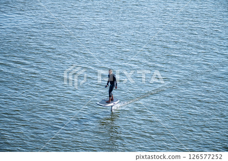 Man on an eFoil board gliding over calm blue water 126577252