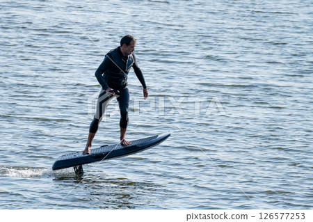Man riding electric hydrofoil surfboard over rippling water 126577253