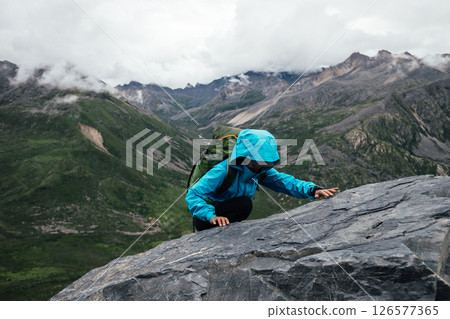 Woman backpacker climbing to steep rocky mountain top 126577365
