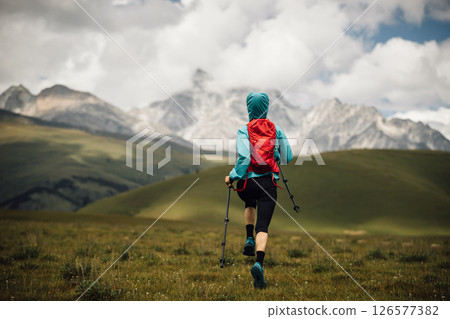 Fitness woman trail runner running in grassland with snow capped mountains in the background 126577382