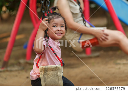 cheerful toddler girl with mother playing on a swing at playground 126577579