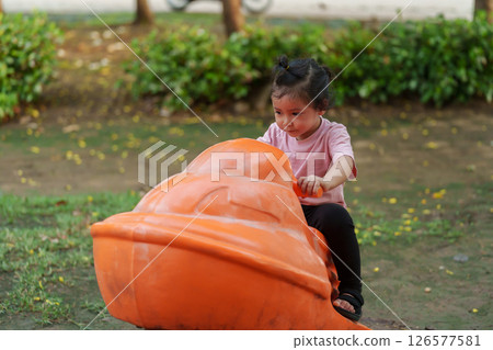 happy toddler girl riding jet ski toy at playground 126577581