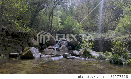 Small waterfall tumbles over mossy rocks into a clear levada 126577718