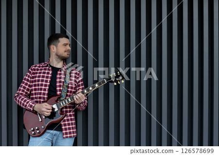 A stylish young guy plays the guitar on a dark background 126578699