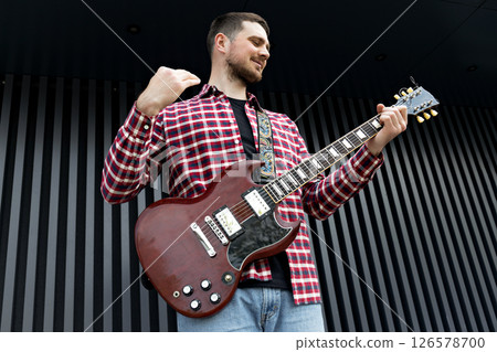 A stylish young guy plays the guitar on a dark background A stylish young guy plays the guitar on a dark background 126578700