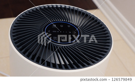 Tall round air purifier with a black top fan and a white body on a tile floor against the wall Tall round air purifier with a black top fan and a white body on a tile floor against the wall 126579849