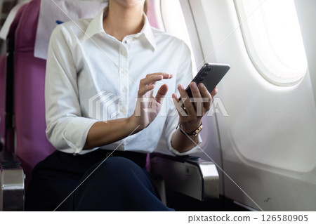 Business Travel. Professional woman using smartphone while seated on an airplane. 126580905