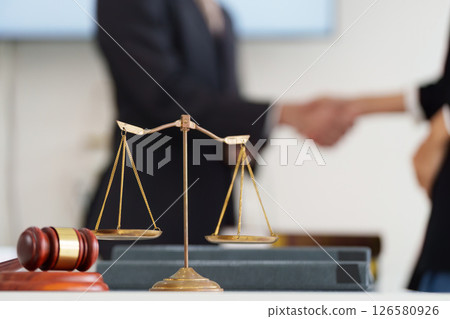 Justice and Legal Balance. A symbolic scale of justice in focus, indicating professionalism during a handshake over legal agreements. 126580926