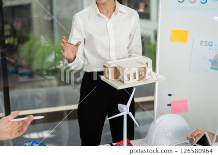Innovative Sustainable Design. Professional showcasing eco-friendly building model during meeting. 126580964