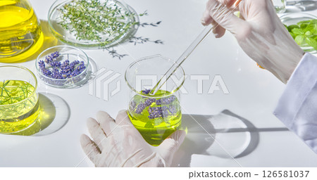 A researcher's hand is stirring a bright green natural oil mixture in a glass beaker with a glass stirring rod, surrounded by fresh and dried herbal ingredients. A researcher's hand is stirring a bright green natural oil mixture in a glass beaker with a glass stirring rod, surrounded by fresh and dried herbal ingredients. 126581037
