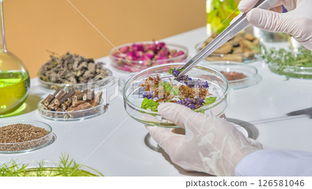 Sorting dried herbal ingredients on white background, surrounded by bottles of essential oil and green extracts. Experimental research with herbs Sorting dried herbal ingredients on white background, surrounded by bottles of essential oil and green extracts. Experimental research with herbs 126581046