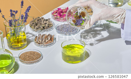 Researcher organizing colorful herbs and extracts for laboratory experiment in organic skincare development. Herbal on lab glassware displayed on white table. Researcher organizing colorful herbs and extracts for laboratory experiment in organic skincare development. Herbal on lab glassware displayed on white table. 126581047