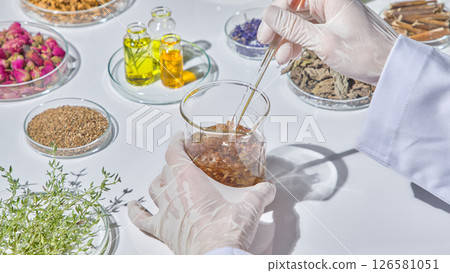 Sorting and arranging dried herbs, seeds and flower petals on a white table for use in organic research. The researcher gently stirs the compound in the beaker with chopsticks. Sorting and arranging dried herbs, seeds and flower petals on a white table for use in organic research. The researcher gently stirs the compound in the beaker with chopsticks. 126581051