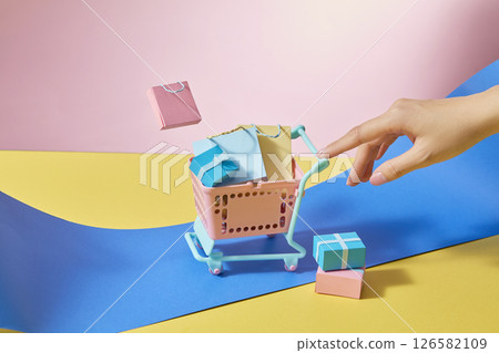 Girl gently pushing a shopping cart filled with colorful shopping bags and boxes. Eye-catching colors of blue, yellow and pink. Conveys convenient shopping, advertising image, design space Girl gently pushing a shopping cart filled with colorful shopping bags and boxes. Eye-catching colors of blue, yellow and pink. Conveys convenient shopping, advertising image, design space 126582109