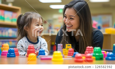 Joyful toddler and smiling teacher play with colorful stacking c 126582392