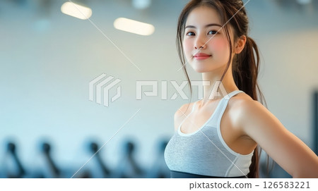 Fit woman smiling confidently in gym, embodying strength and determination. 126583221