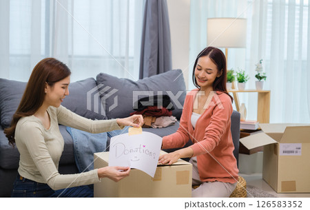 group of friend  sorting and packing clothes into a donation box.community support, and charitable giving 126583352