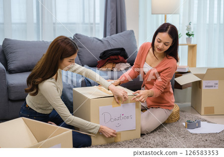 group of friend  sorting and packing clothes into a donation box.community support, and charitable giving 126583353