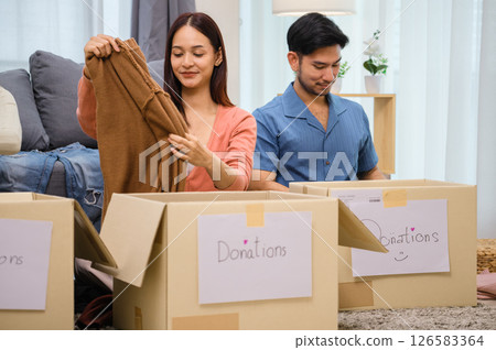 group of friend  sorting and packing clothes into a donation box.community support, and charitable giving 126583364