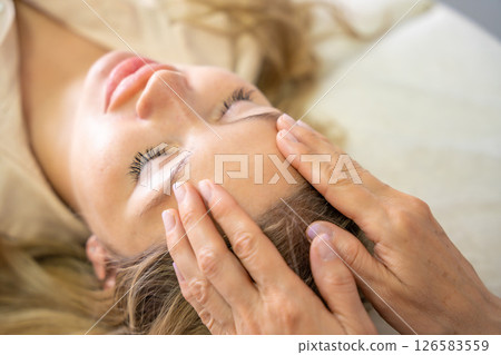 Hands of a female practitioner positioned on the face of a young woman during an Access Bars facial lifting session. Concept of energy work, healing touch and alternative face therapy Hands of a female practitioner positioned on the face of a young woman during an Access Bars facial lifting session. Concept of energy work, healing touch and alternative face therapy 126583559
