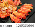 Peeled Hanasaki crab meat is lined up on a black plate, the meat served in its shell. 126583699