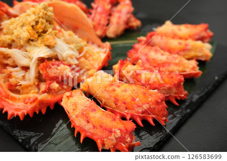 Peeled Hanasaki crab meat is lined up on a black plate, the meat served in its shell. 126583699