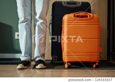 Close up of woman wearing jeans and shoes standing near suitcase ready to leaving home for travel. Female feet and luggage near door before departure 126583837