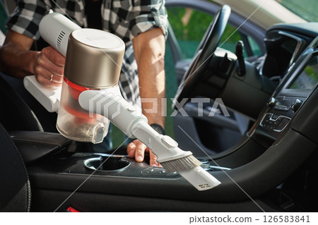 Man is vacuuming dirty car interior using handheld cordless vacuum cleaner. Car owner care about vehicle, cleaning seat upholstery and interior . Vehicle daily cleaning for comfort and hygiene 126583841