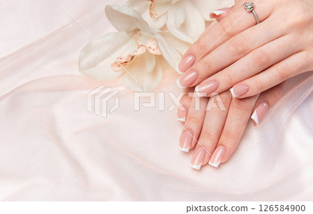Woman showing french manicure and diamond ring near orchid flower 126584900