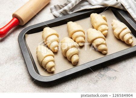 Raw croissants baking on tray with rolling pin and kitchen towel 126584904