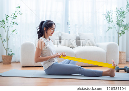 Young Asian woman doing pilates workout using elastic strap pulling with arms 126585104