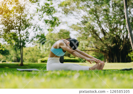 Young Asian woman doing yoga stretching on green grass 126585105
