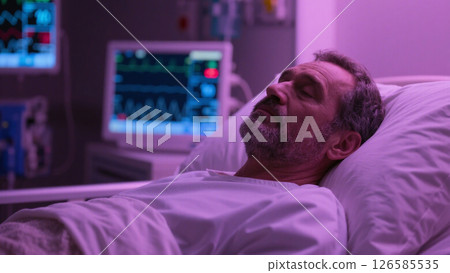 A middle-aged man with a short beard lying peacefully in a hospital bed, wearing a white patient gown. 126585535