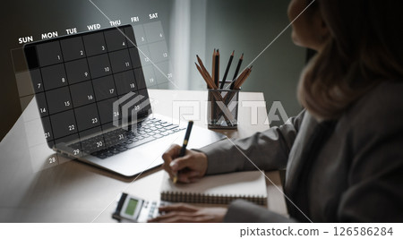 2025 calendar person planning or scheduling on laptop with calendar overlay, working at desk with stationery and calculator, in bright room 126586284